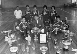 体育館で優勝カップを囲む監督と選手の集合写真