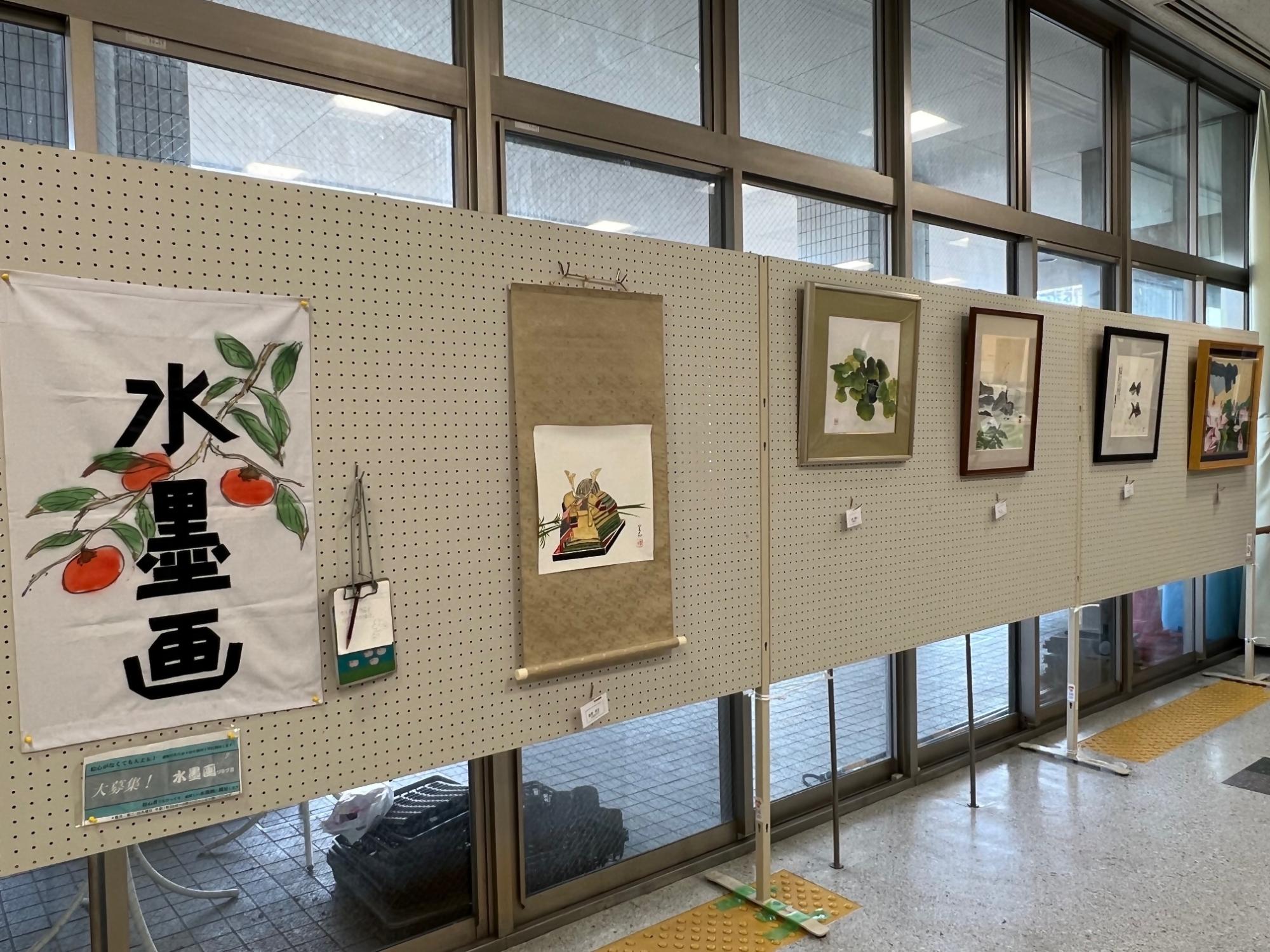 水墨画クラブのロビー展示の様子です。兜、花、海などが鮮やかな水墨画で描かれています。