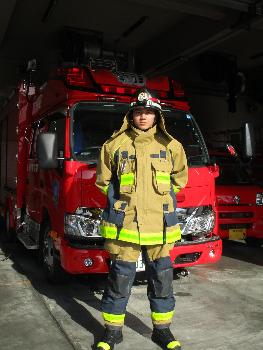 消防車の前で防火服を着た消防職員が立っている様子です。