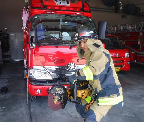 消防車の前で防火服を着た消防職員がエンジンカッター(金属などを切きるための道具)を持っている様子です。