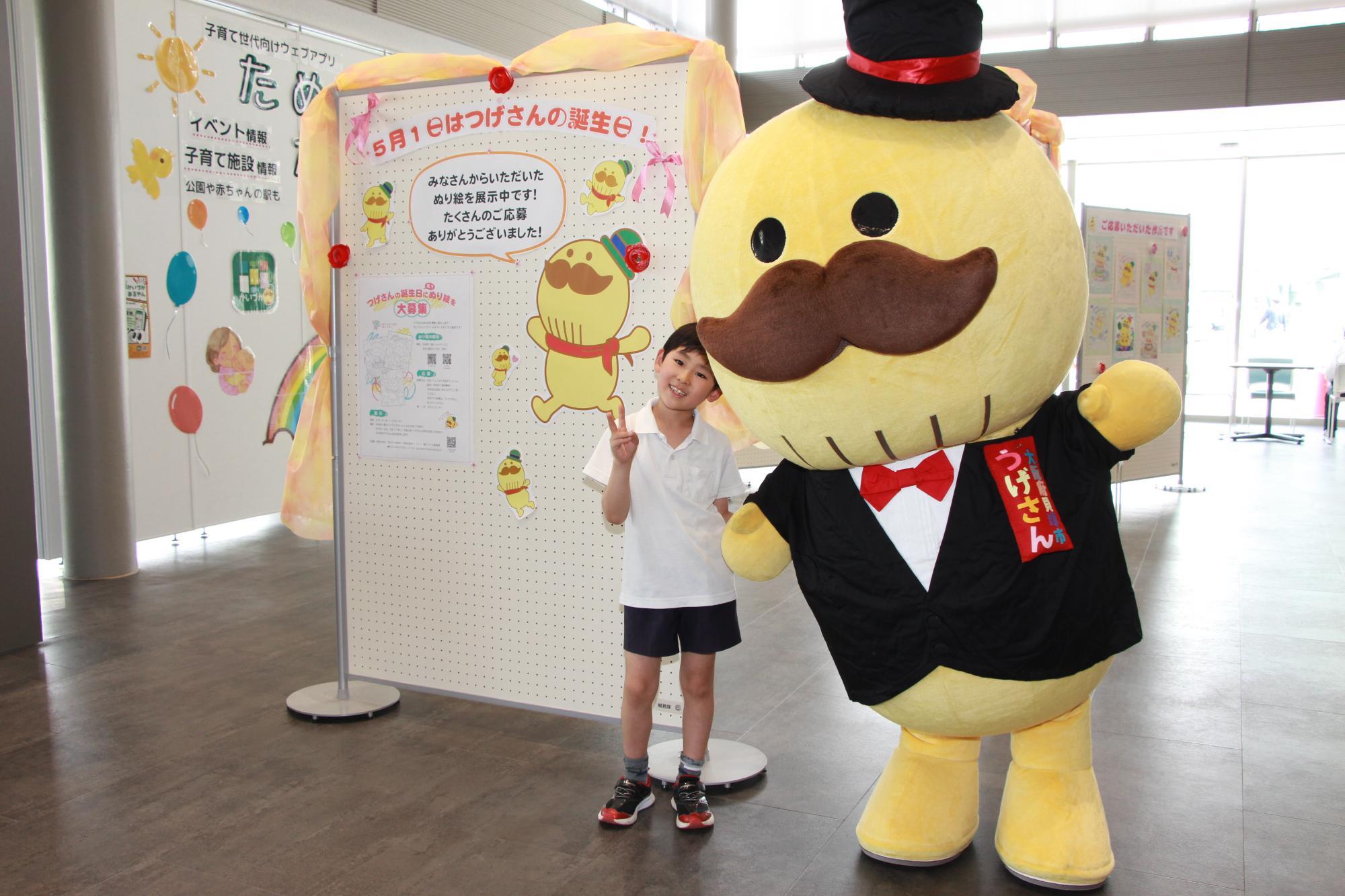 展示作品の前でポーズをとるつげさんと小学生の写真です