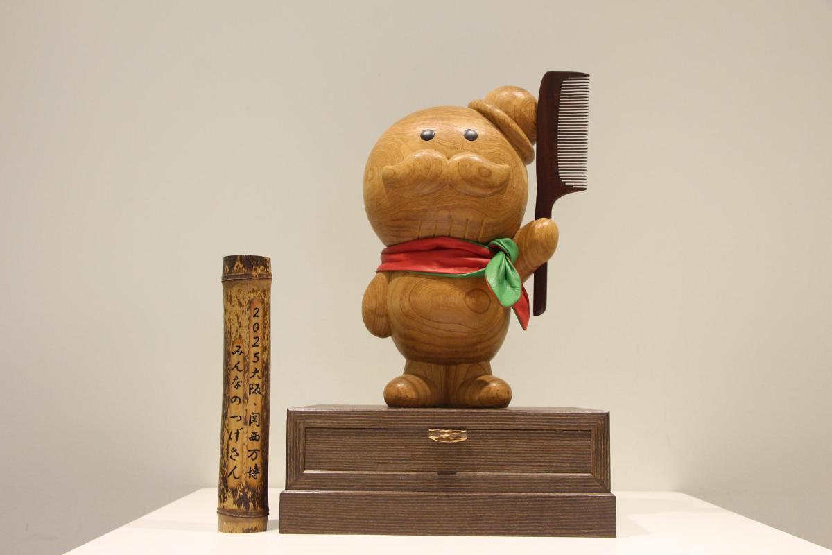 手につげ櫛を持った木彫りのつげさんが台座に立っている写真です
