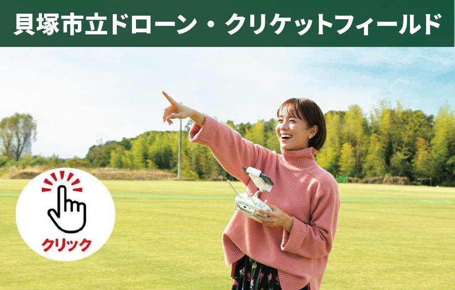 貝塚市立ドローン・クリケットフィールドについてのページです。詳しくはこちらをクリックしてください。（ドローンのコントローラーを片手に持ち、空に飛ぶドローンを指差しする笑顔の女性の写真あり）