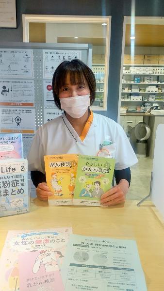 あんず薬局がん検あんず（薬局のカウンターでがん検診やがんの知識に関するパンフレットを手に持っている人の写真）