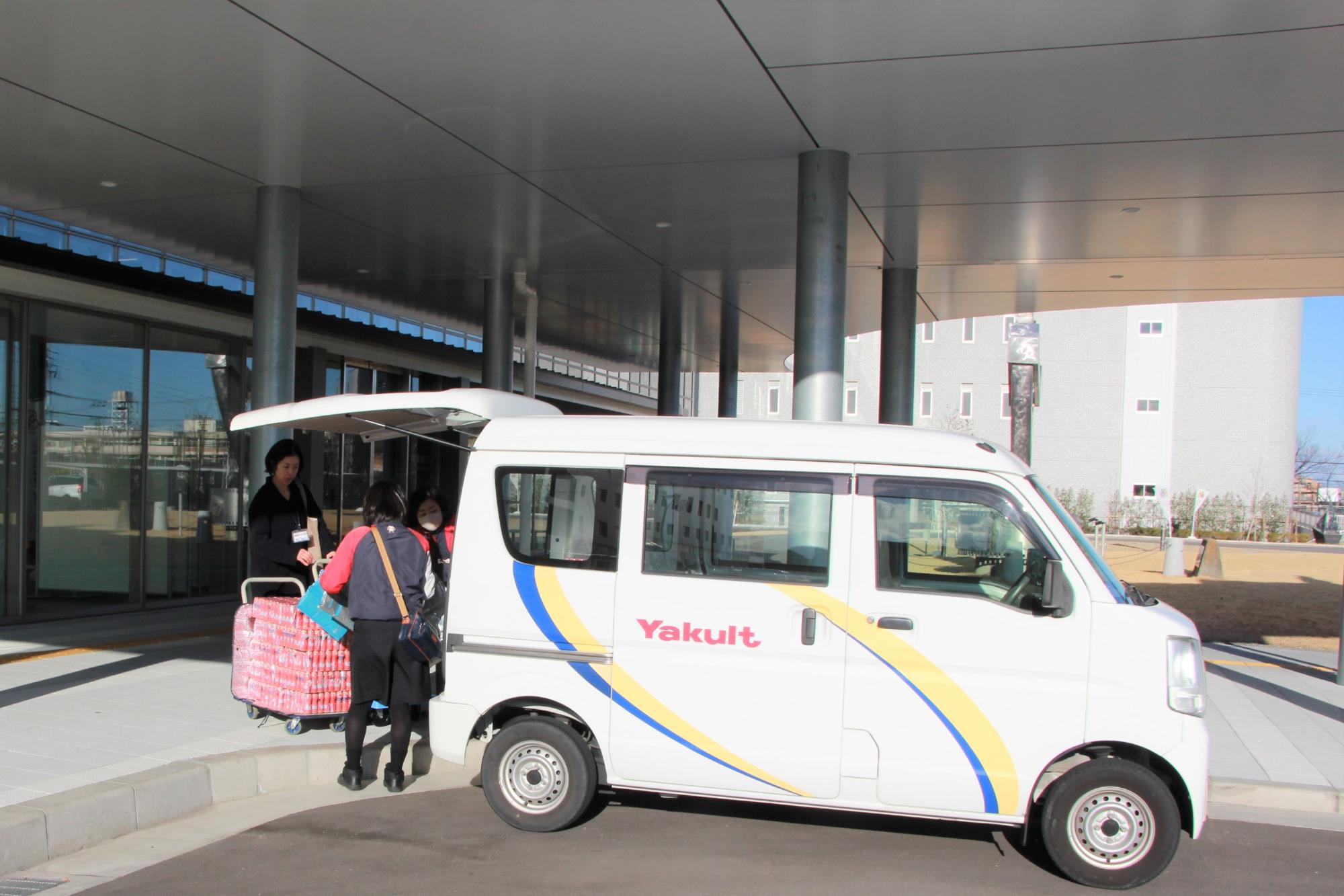 ヤクルト搬入（「Yakult」のロゴが入った搬入車を貝塚市役所エントランス付近に停めてヤクルトを荷下ろしし、台車に積む様子）