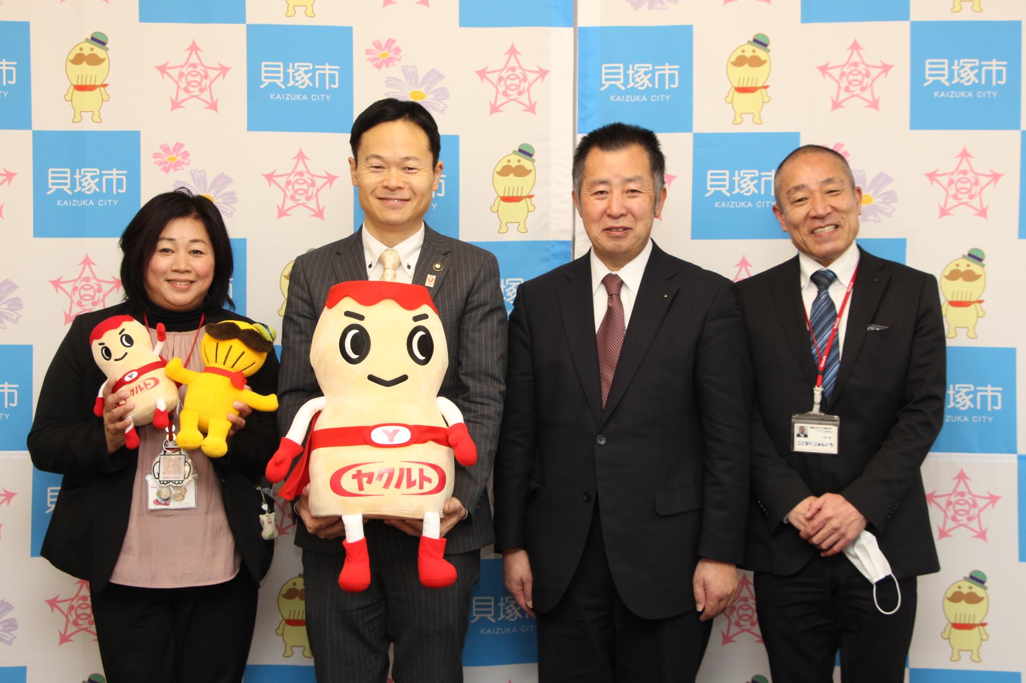 近畿中央ヤクルト販売株式会社感謝状贈呈（近畿中央ヤクルト販売株式会社代表取締役社長湯澤様、営業統括部大阪・泉州営業所統括部長小泊様、泉州エリア担当部長信貴様、貝塚市酒井市長が並んで写真撮影  ヤクルトマンやつげさんのぬいぐるみを手に持っている）