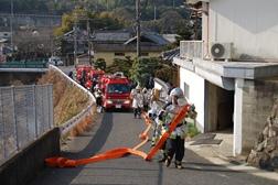 消防車からホースをのばし坂道を駆け上がる消防隊員のようすの写真