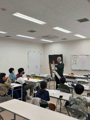 講師が植物の種を手に持ち説明し、子どもが着席して受講している様子