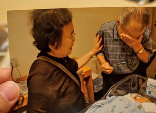 令和2年度かいづか家族の日の写真部門優秀賞作品です 生まれたての赤ちゃんを見て涙をぬぐう祖父と 祖父の肩に手を添える祖母の様子を写した写真です
