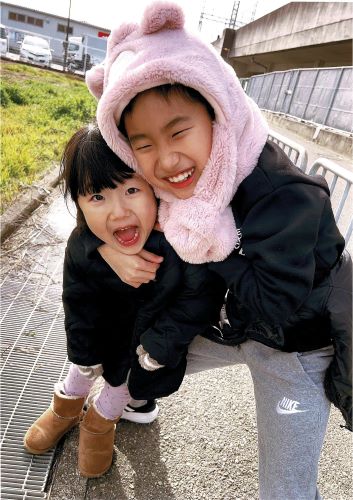 兄が妹の帽子をかぶり、背後から抱きしめて二人とも笑顔で写っている写真です。