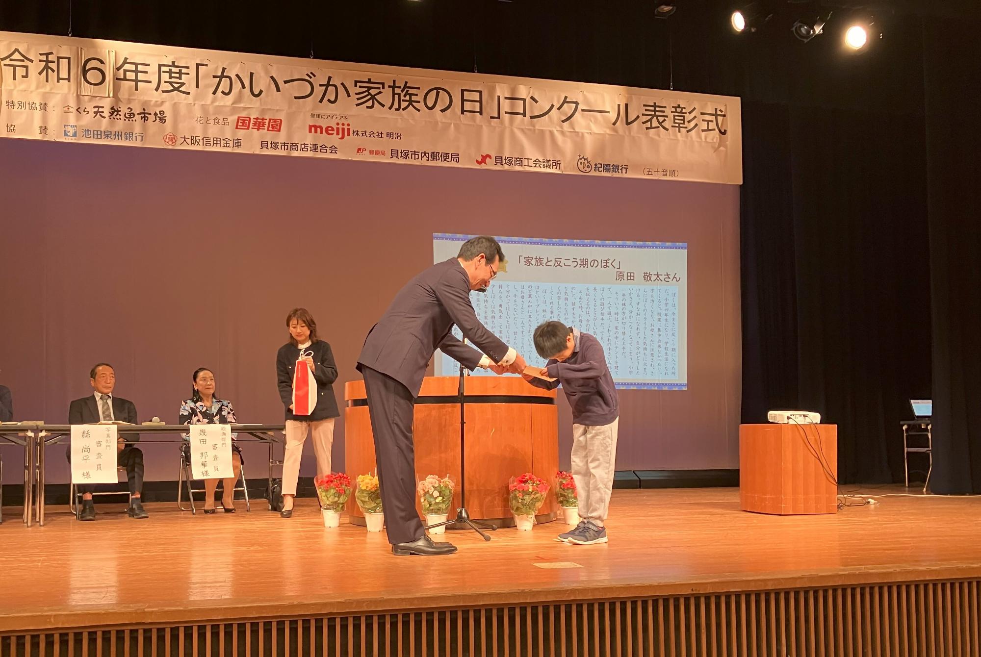 教育長がエッセイ部門の最優秀賞受賞者に表彰状を授与している様子です。
