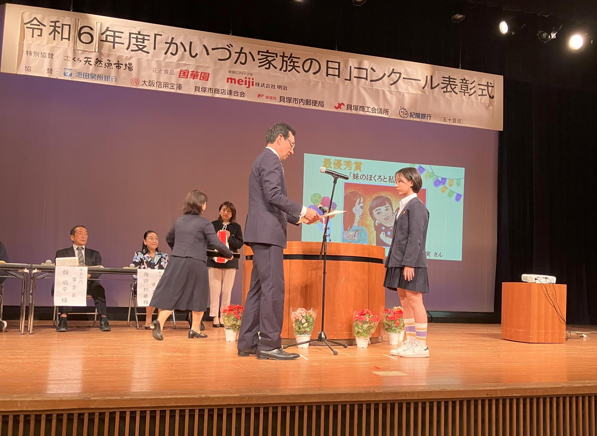 教育長が絵画部門の最優秀賞受賞者に表彰状を授与している様子です。