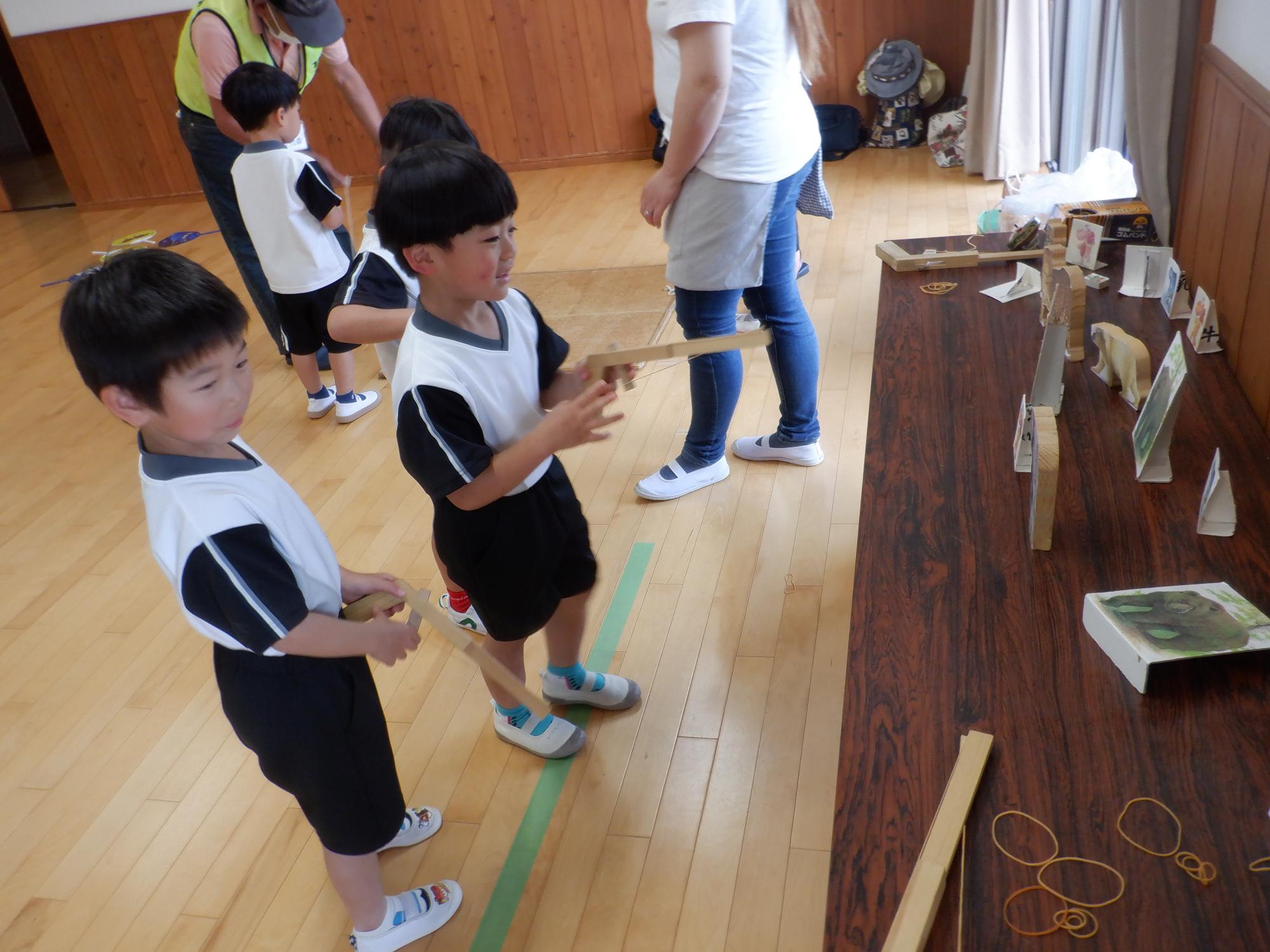 子どもたちが机の上の的に向かってゴム銃を撃って遊んでいる様子