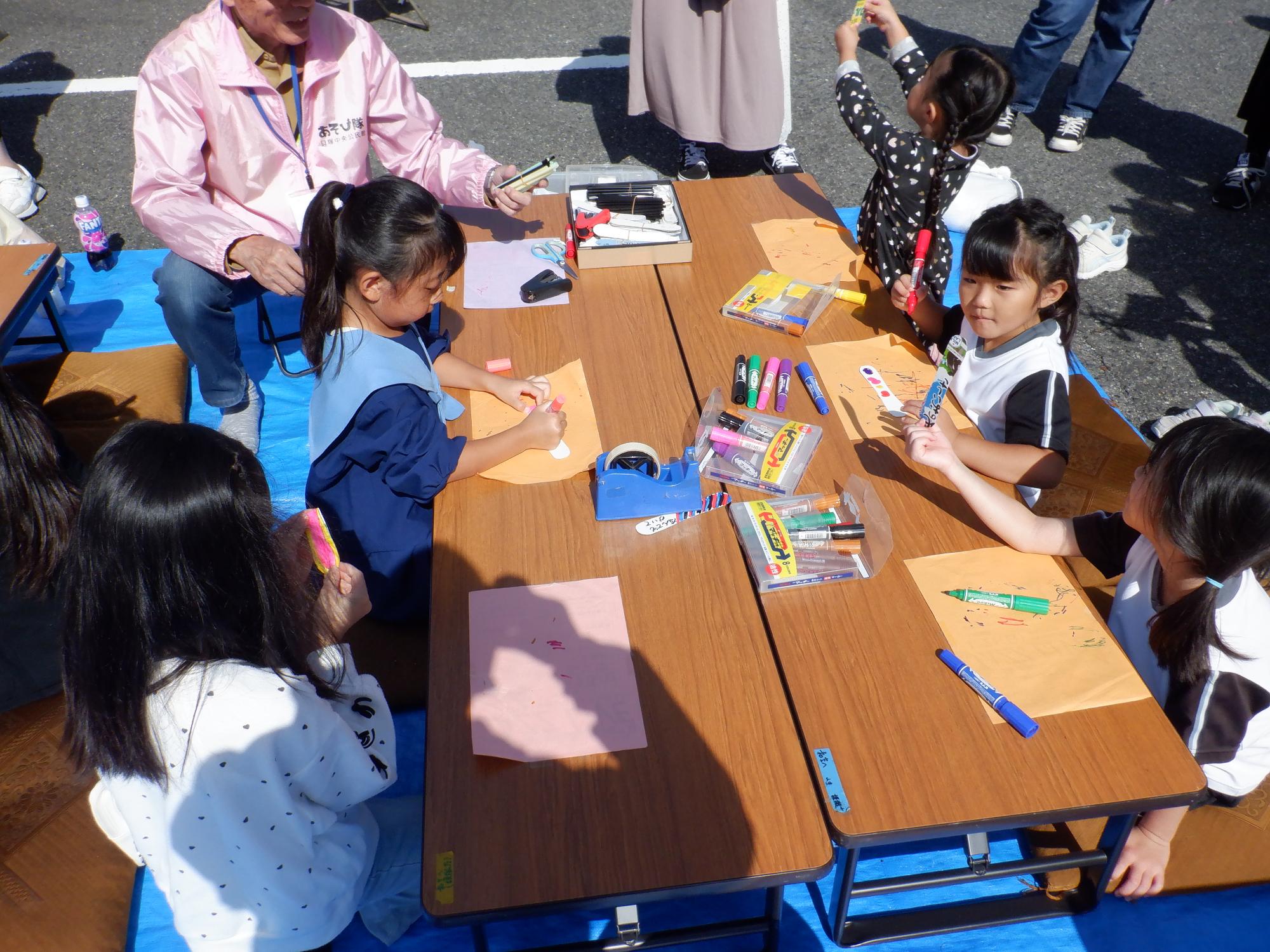 子どもたちが、オレンジ色やピンク色の紙に油性マーカーペンで色をぬっている様子