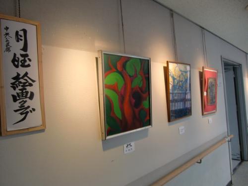 月曜絵画クラブの作品展（色とりどりの絵画が廊下の壁に掛けて飾られている）