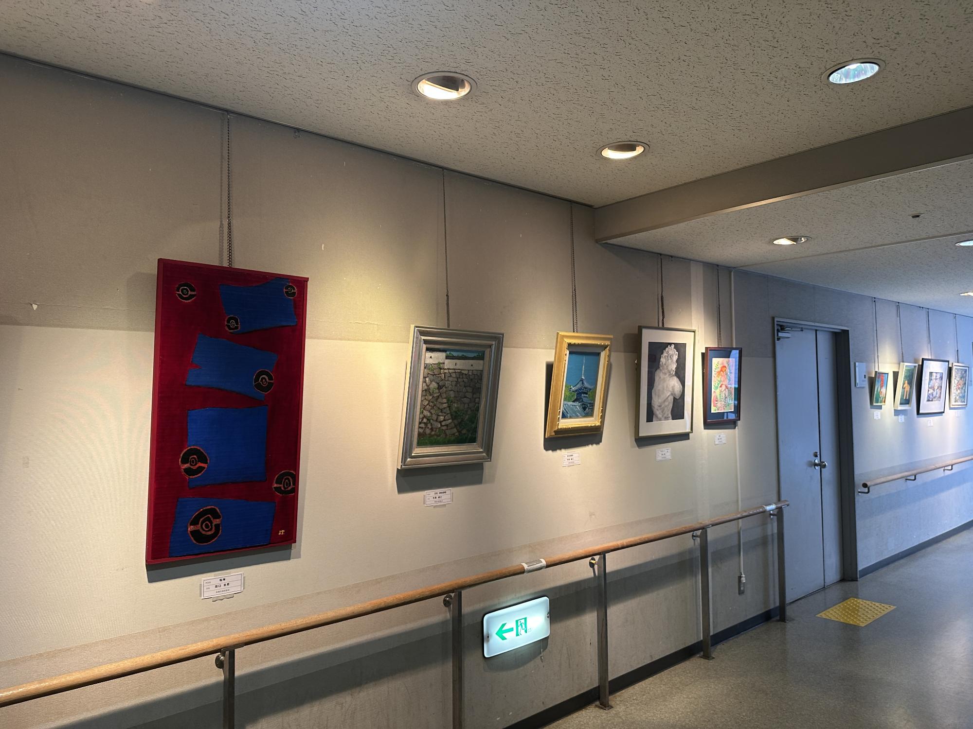 公民館のロビーの壁にさまざまな大きさの絵画の作品が飾られている