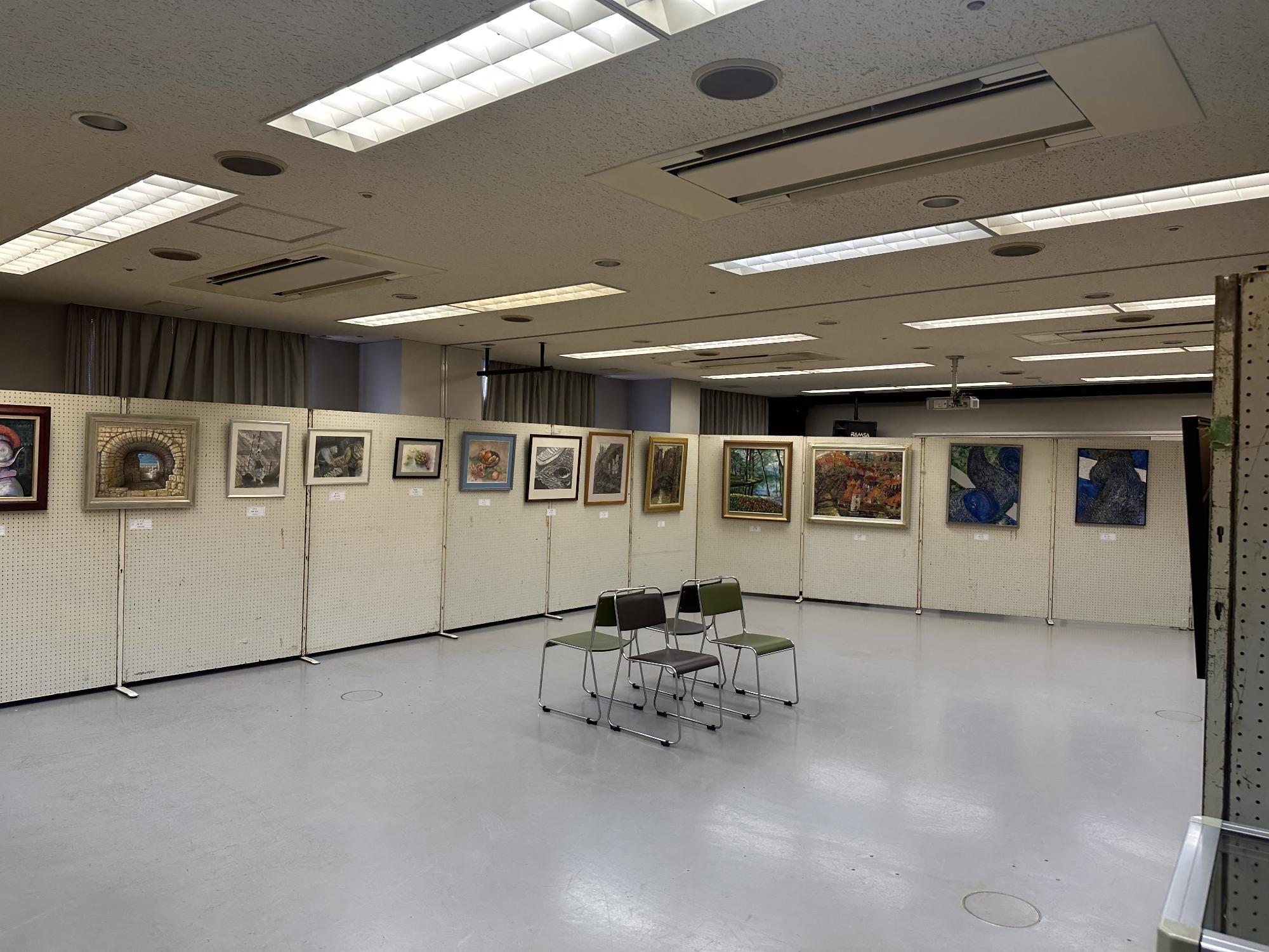 大きい部屋にパネルが四方に並び、そのパネルに多数の絵画作品が並び、真ん中にイスがある