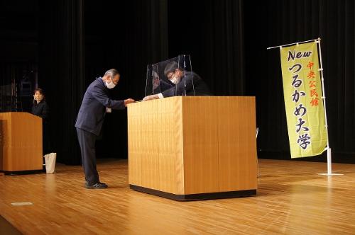 修了証書授与の様子です  舞台上には「つるかめ大学」の文字が書かれたのぼり旗が設置されています