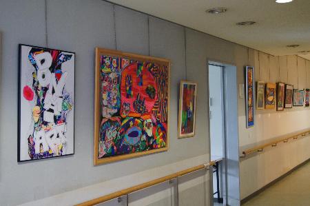 にっこり展の作品（色とりどりの絵画が廊下の壁に掛けて飾られている）