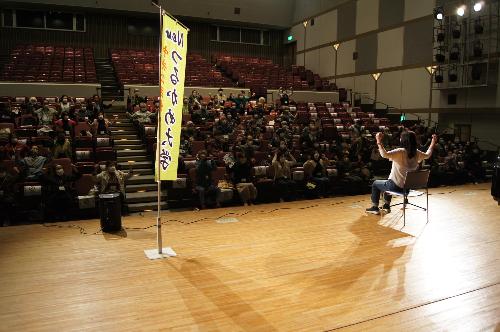 つるかめ大学の開講式の様子です  舞台上には「つるかめ大学」の文字が書かれたのぼり旗が設置されています