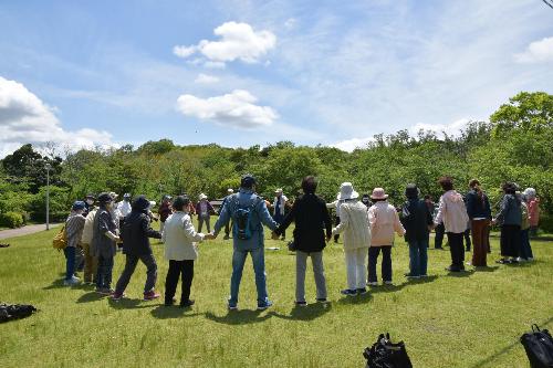 つるかめ大学のハイキングの様子です  たくさんの参加者が輪になって手をつないでいます