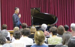 宮崎剛さんがグランドピアノの前に立って、会場のみなさんに向けてお話しています。