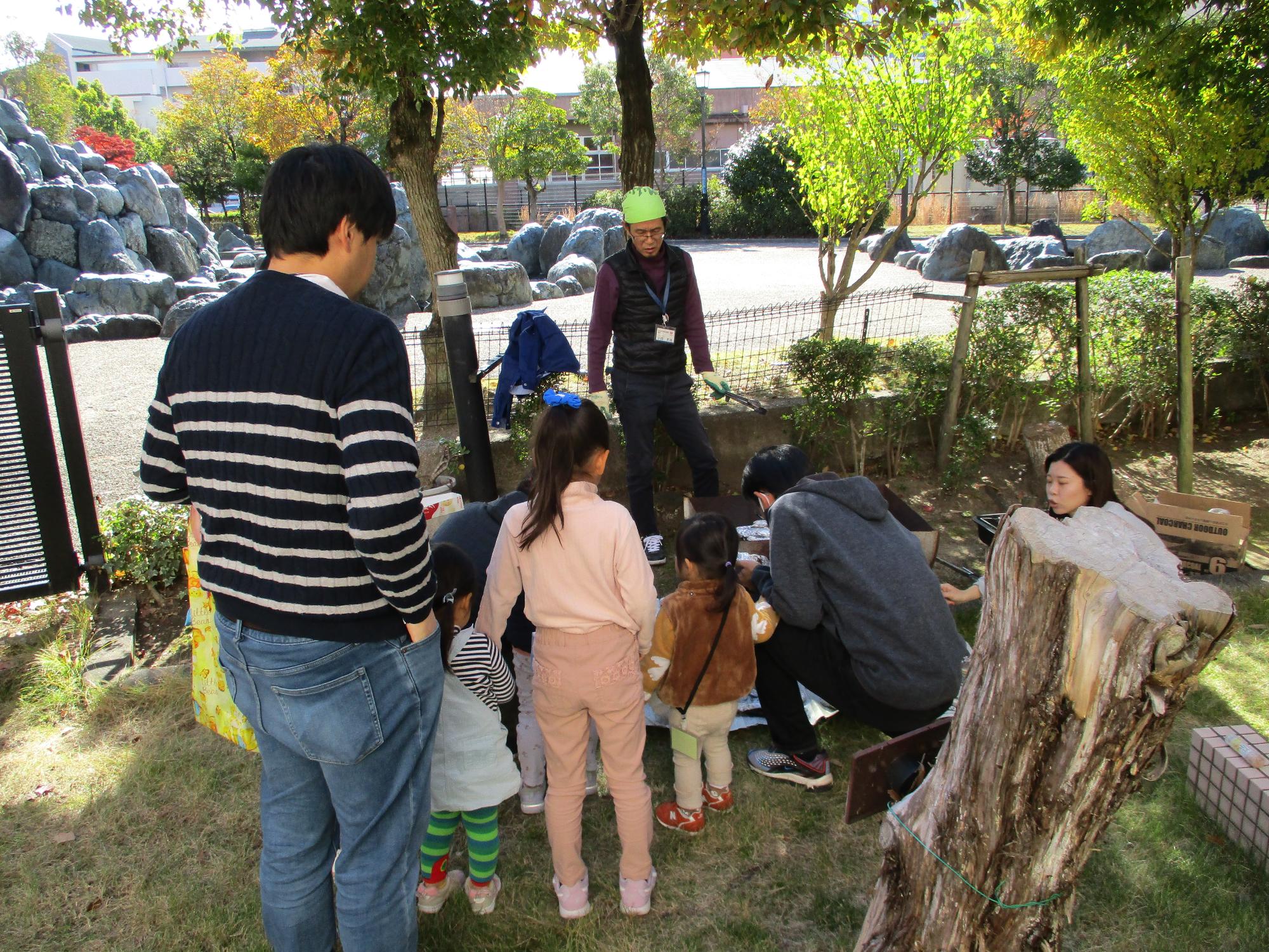 お父さんと子ども達が、新聞紙に包んださつまいもが焼ける様子をのぞき込んでいます。