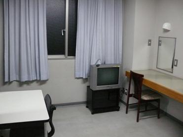 楽屋（洋室）の写真（壁掛けの鏡の前に壁掛けテーブルと椅子がある  その他、デスク、チェア、テレビが置かれている）