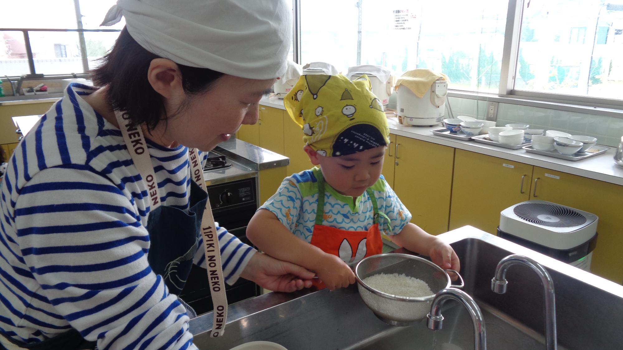 親子で料理をする様子（子どもがお米を研ぐのをお母さんが手伝っています）