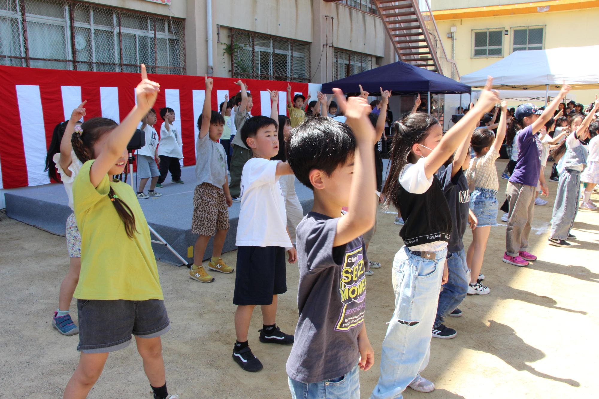 子どもまつり舞台発表の様子(子どもたちが片手を高く指差ししてポーズをとっています。）