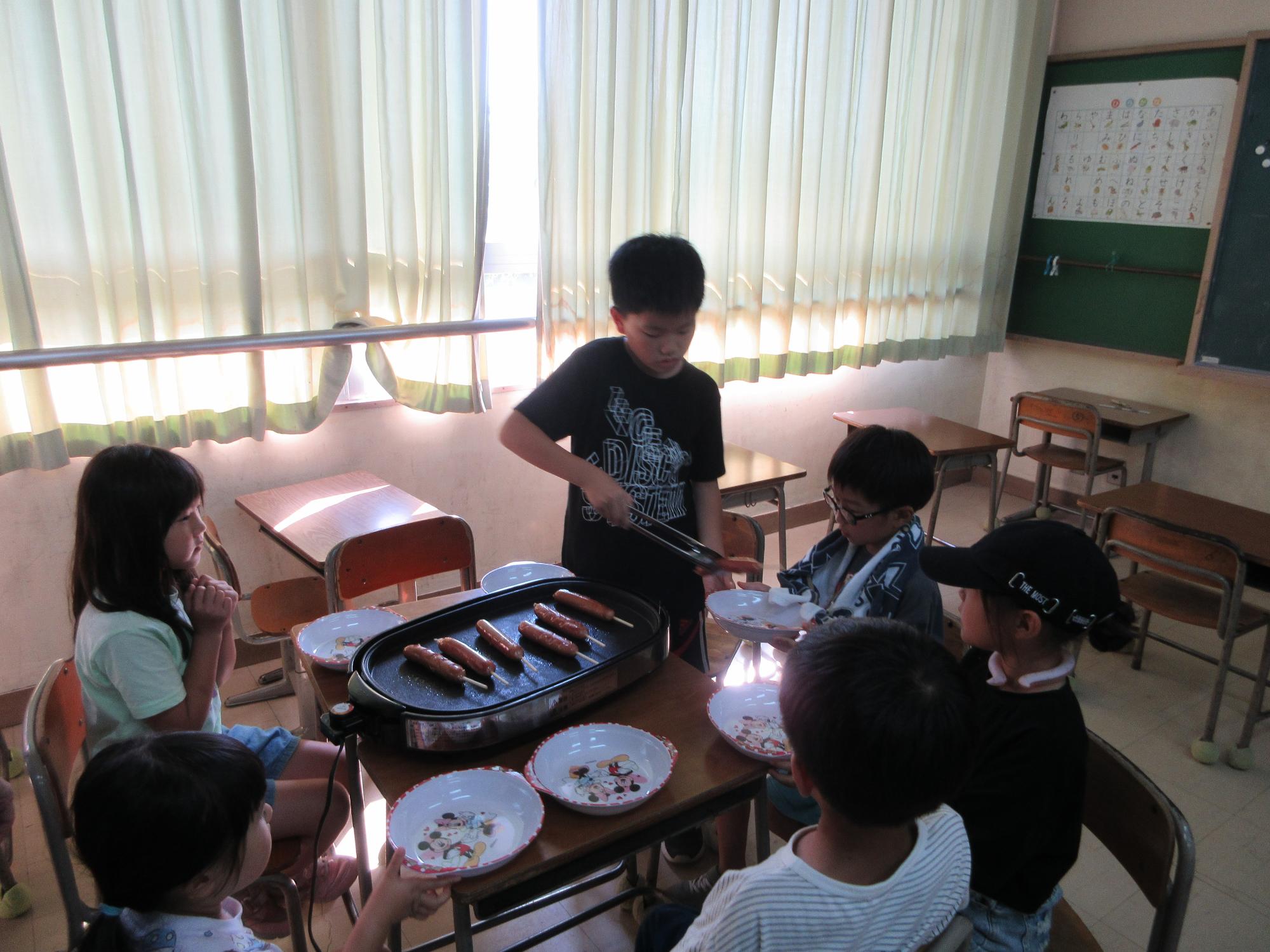 子どもたちがフランクフルトをホットプレートで焼いている様子