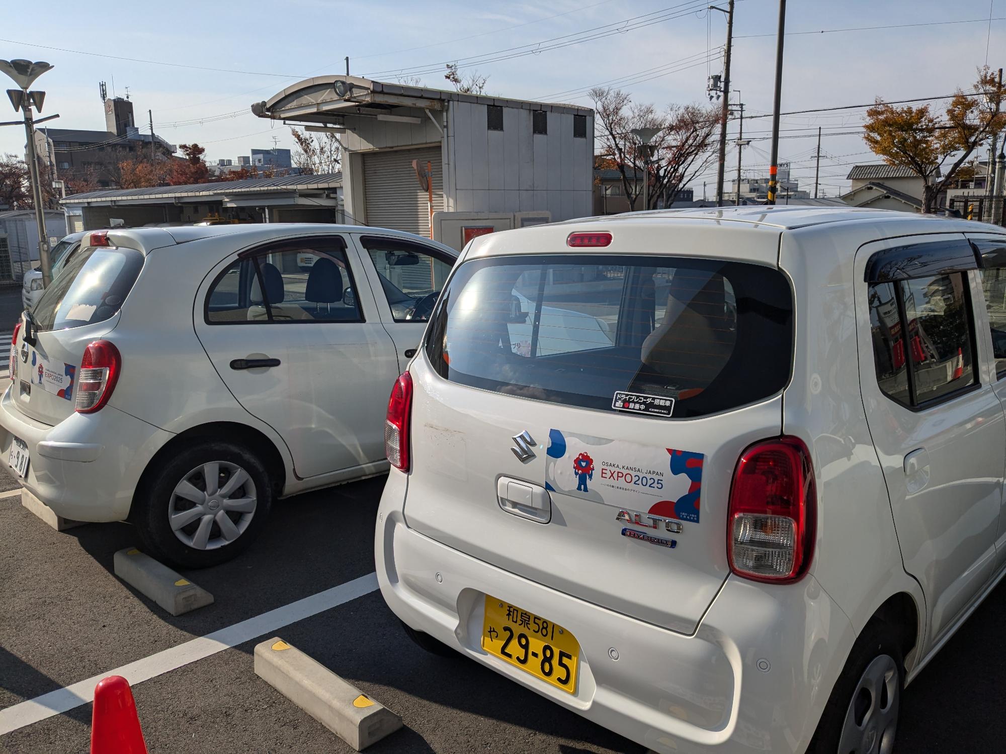 公用車を右側後方から撮影した写真です。後部ドア右側に「大阪・関西万博」機運醸成のためのステッカーを貼付しています。ステッカーには「EXPO2025」の文字と、関西万博公式キャラクター「ミャクミャク」のイラストが描かれています。