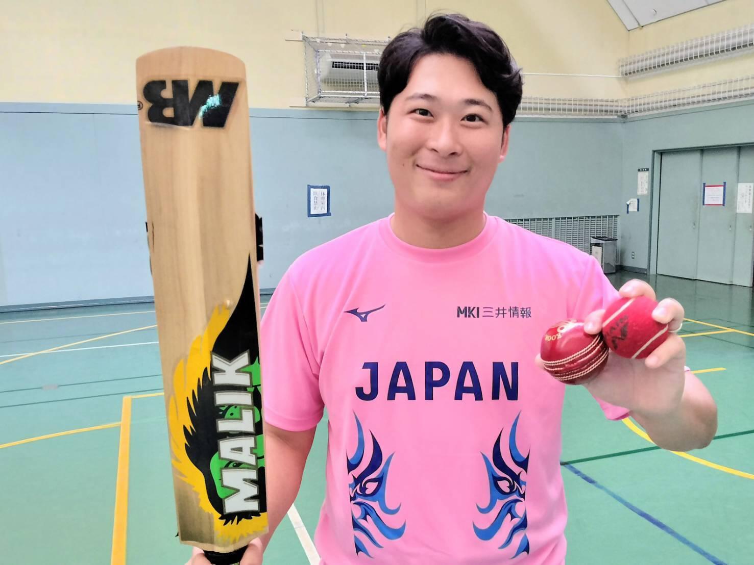 クリケット日本代表レプリカユニフォームを着た職員がクロケット用バットとボールを持っています
