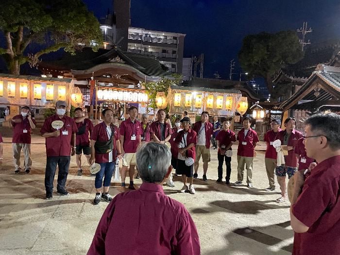 えんじ色のTシャツを着用した青少年指導員たちが太鼓台祭りの巡回パトロールのため集合している様子（夜）