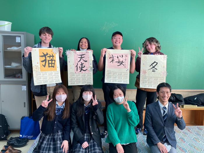 カルバーシティ市の高校生たちが貝塚高校書道部の生徒、先生たちと集合写真を撮影しました。（カルバーシティ市の高校生たちは毛筆で書いた文字の紙を手に持っている  左の生徒から順に「猫」「天使」「桜」「冬」の字）