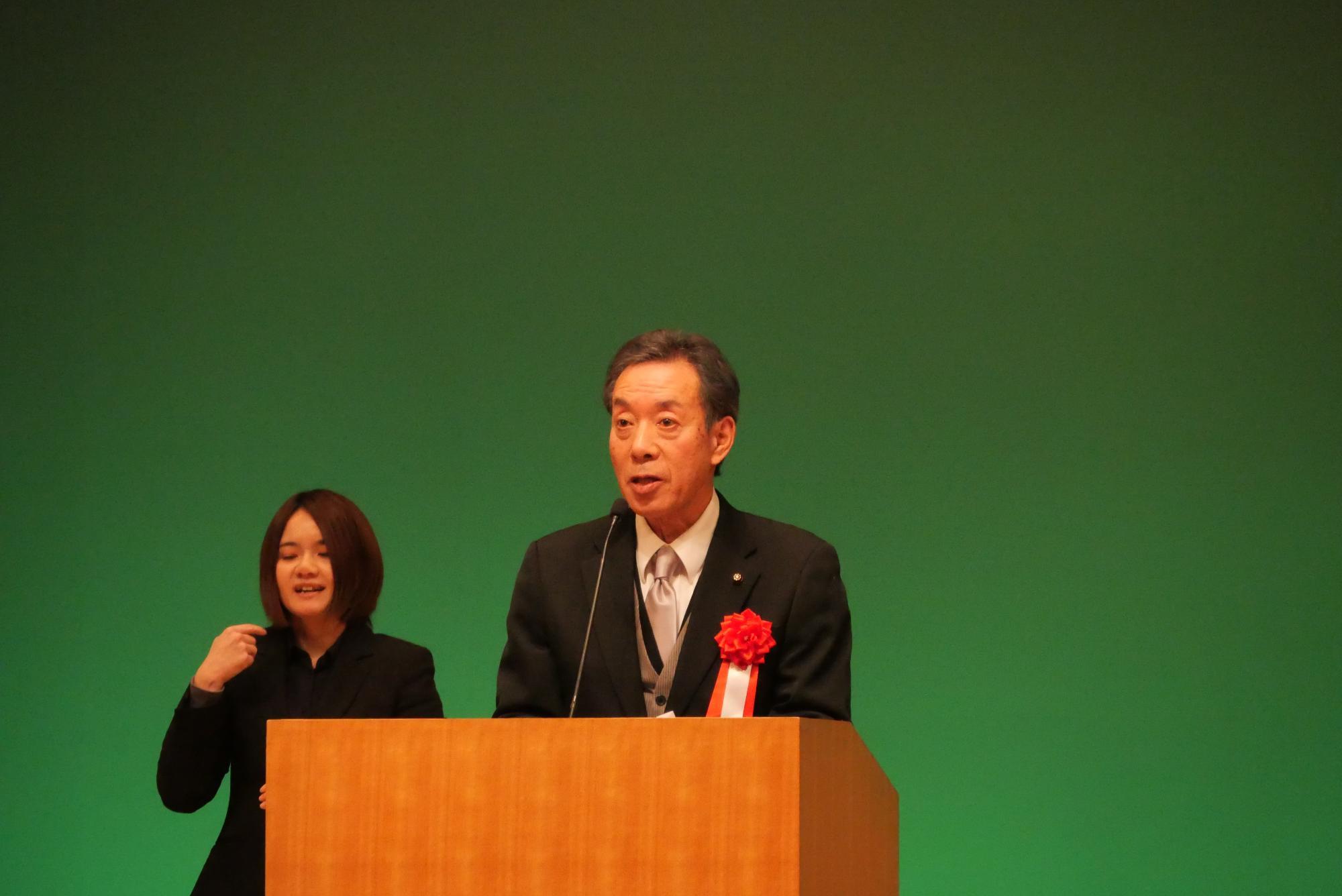 コスモスシアター大ホール舞台上にて市議会議長があいさつをしている様子