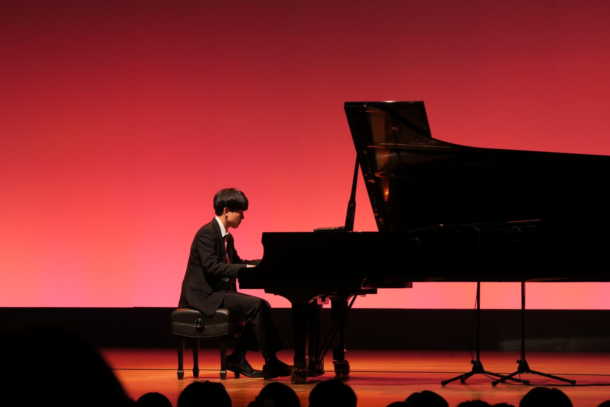 コスモスシアター大ホール舞台上にて第2部のパフォーマンスとして新20歳の男性がピアノ演奏をしている様子