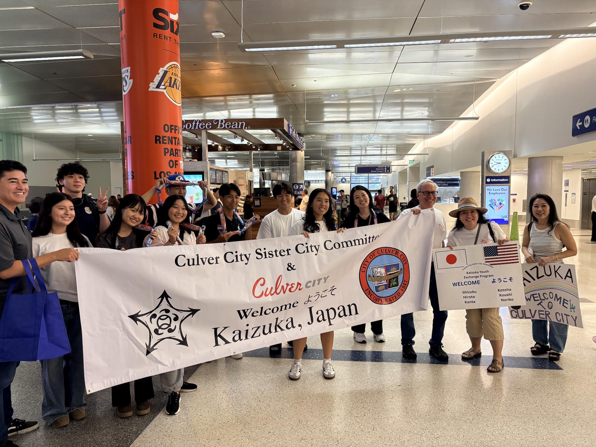 ロサンゼルス空港で「ようこそ貝塚」と書かれている旗をもち写真を撮っている様子。