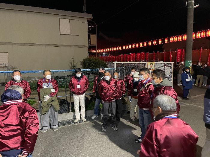 えんじ色の上着を着用した青少年指導員たちが十日戎街頭指導のため集まっている様子（夜）