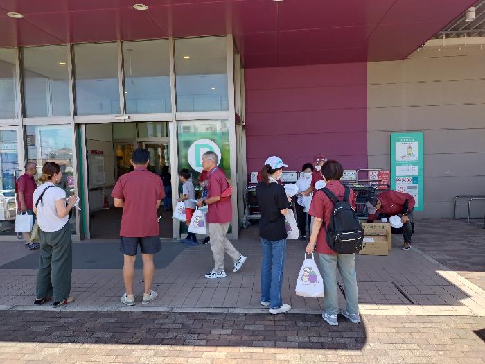 ショッピングセンターの入り口前で、えんじ色のTシャツを着用した青少年指導員たちが社会を明るくする運動街頭啓発活動をしている様子