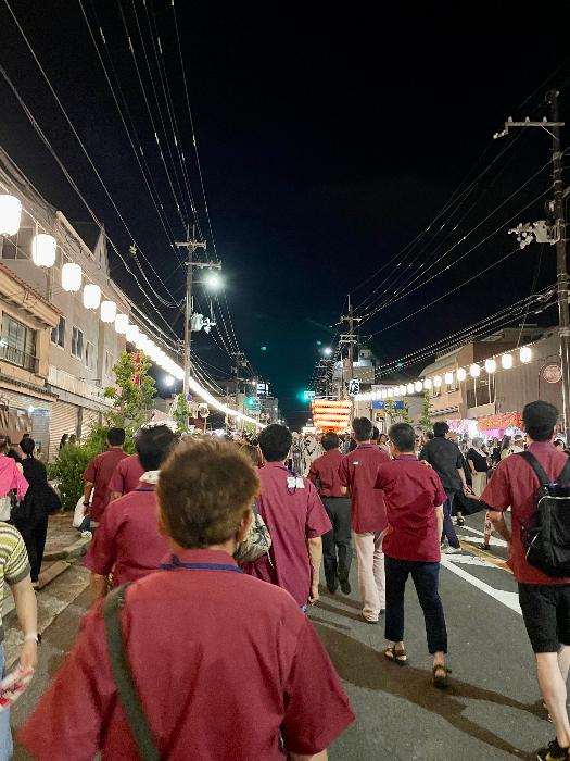 えんじ色のTシャツを着用した青少年指導員たちが太鼓台祭りの巡回パトロールをしている様子（夜）