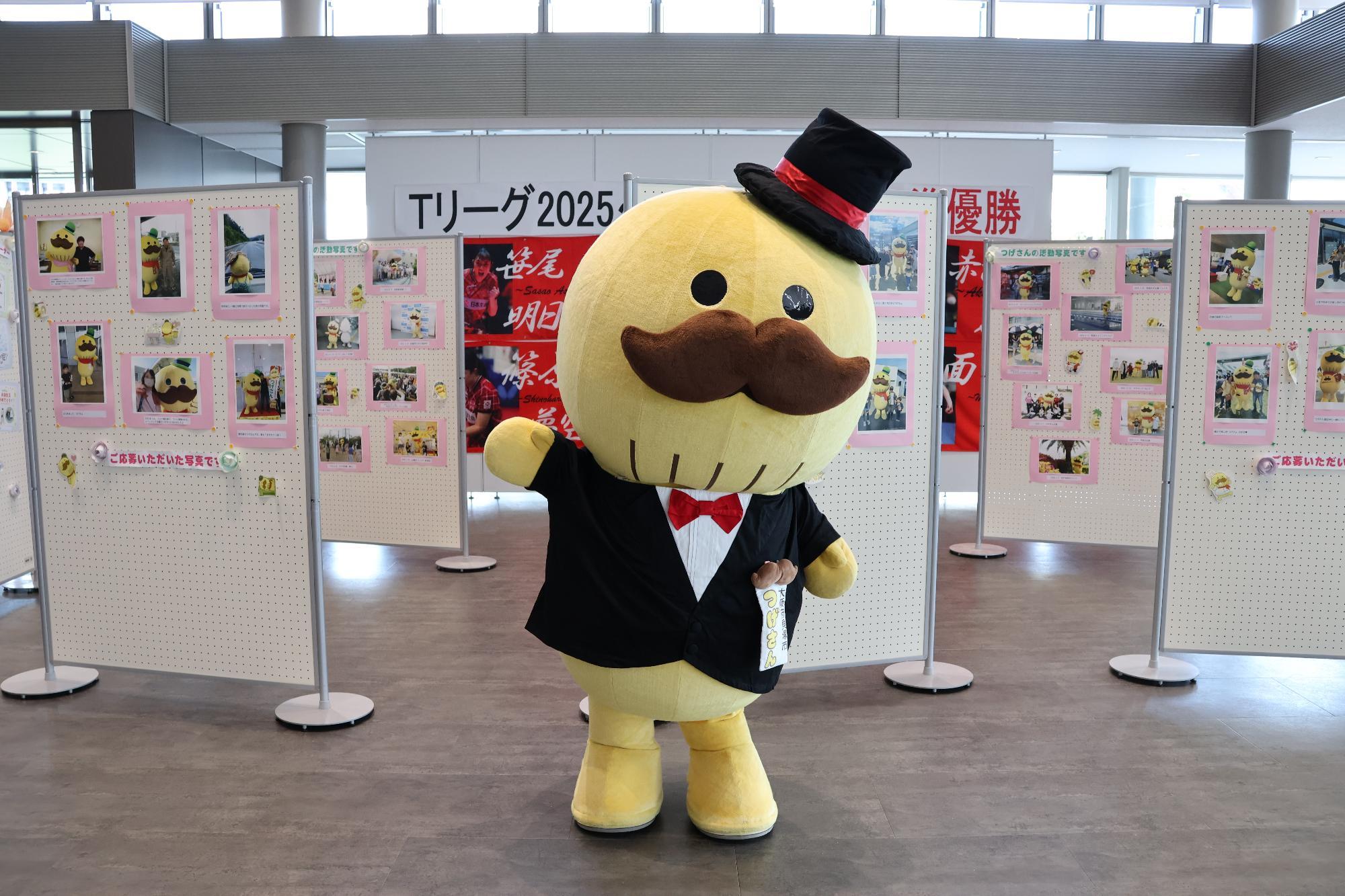 つげさんが写真展の前でポーズをしている写真です