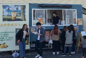 青色のキッチンカーの左手にわかやまジュースの看板を掲げており、行列が出来ている様子。