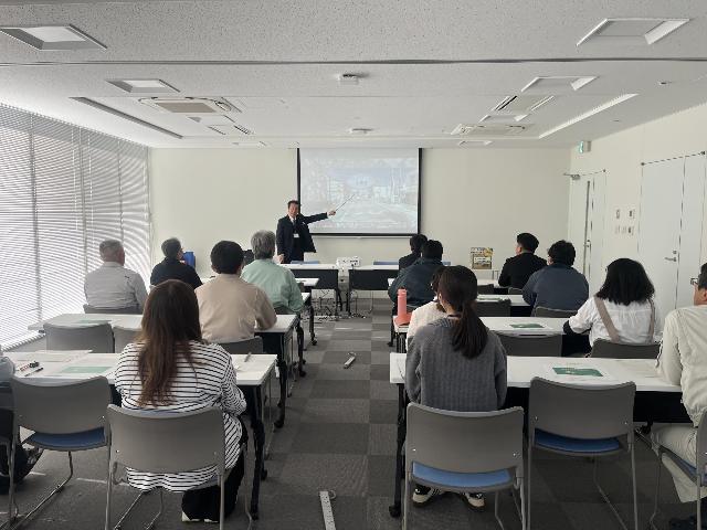 市職員を対象に、関西自動車学院の講師が座学講義をしている様子。会場前方のスクリーンには、講義内容のスライドが映し出されています。